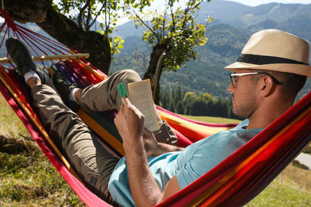 Handsome man reading book in hammock outdoors on sunny dayの写真素材
