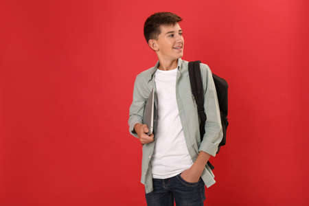 Teenage student with backpack and laptop on red backgroundの写真素材