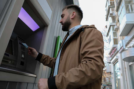 Man inserting credit card into cash machine outdoors, low angle viewの写真素材