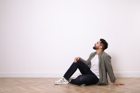 Young man sitting on floor near white wall indoors. Space for textの写真素材