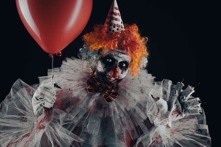 Terrifying clown with red air balloon on black background. Halloween party costumeの写真素材