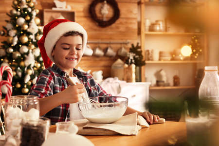 Cute little boy in Santa hat making dough for Christmas cookies at homeの写真素材