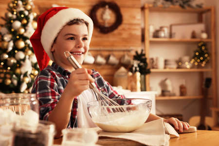 Cute little boy in Santa hat making dough for Christmas cookies at homeの写真素材