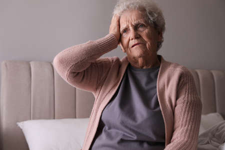 Senior woman with headache in bedroom at homeの写真素材