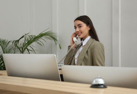 Beautiful receptionist talking on phone at counter in hotelの写真素材