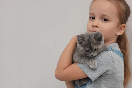 Cute little girl with kitten on light background, space for text. Childhood petの写真素材