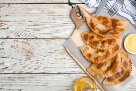 Delicious fried chebureki with sauce on white wooden table, flat lay. Space for textの写真素材