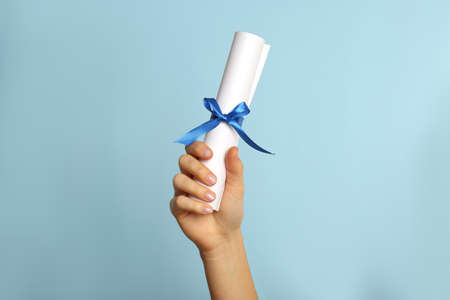 Student holding rolled diploma with ribbon on light blue background, closeup
