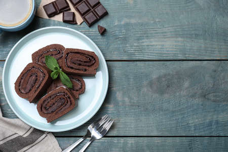 Tasty chocolate cake roll with cream and mint on blue wooden table, flat lay. Space for textの写真素材