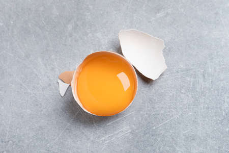 Cracked eggshell with raw yolk on light gray table, top view