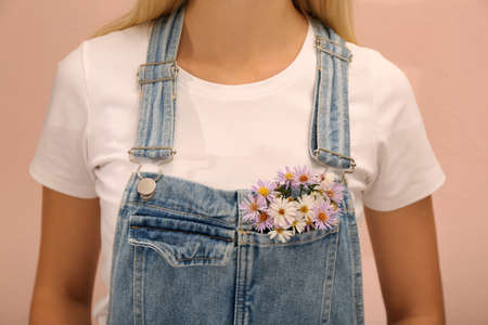 Woman with beautiful tender flowers in denim jumpsuit's pocket on pale orange background, closeup