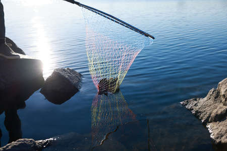 Fisherman holding fishing net with catch at riverside, closeup
