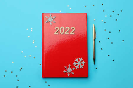 Red planner, pen, decorative snowflakes and confetti on light blue background, flat lay. Planning...