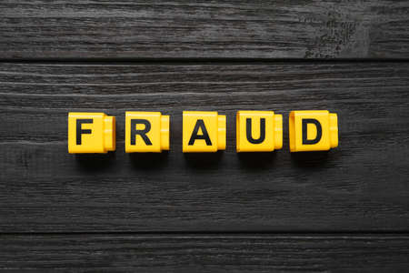 Word Fraud of yellow cubes with letters on black wooden background, flat layの写真素材