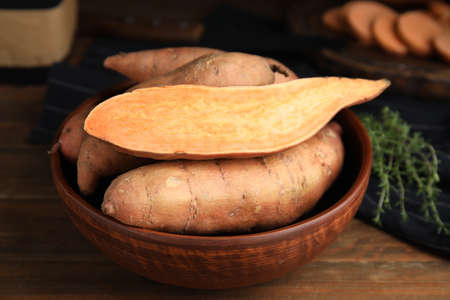 Cut and whole sweet potatoes in bowl on wooden table, closeupの写真素材
