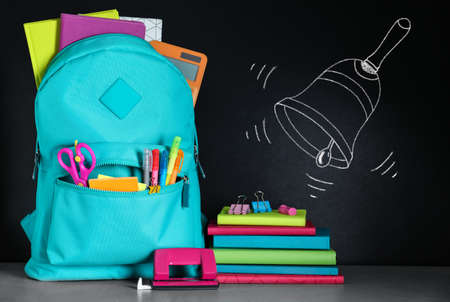 Backpack full of stationery near blackboard with drawn school bellの写真素材
