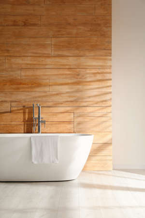 White bathtub with towel near wooden wall in roomの写真素材
