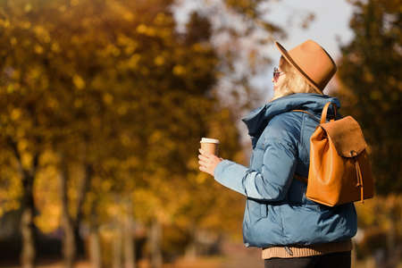 Young woman with stylish backpack and hot drink on autumn day, space for textの写真素材