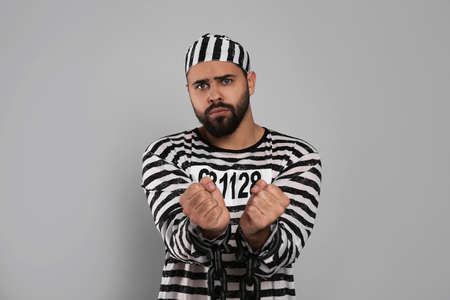 Prisoner in special uniform with chained hands on gray background