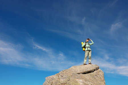 Young woman with backpack on rocky peak in mountains. Space for textの写真素材