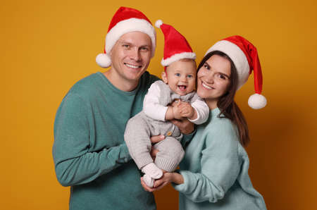 Happy couple with cute baby wearing Santa hats on yellow background. Christmas seasonの写真素材