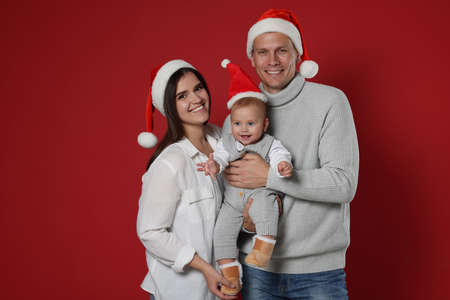 Happy couple with cute baby wearing Santa hats on red background. Christmas seasonの写真素材