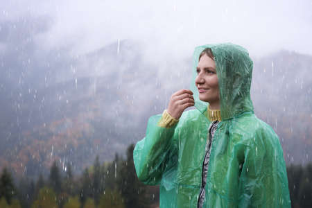 Young woman in raincoat enjoying mountain landscape under rainの写真素材