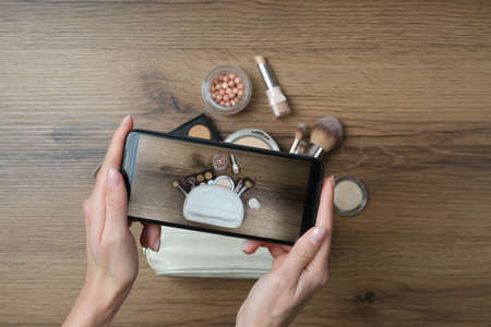 Woman taking photo of makeup products with smartphone at wooden table, top viewの写真素材