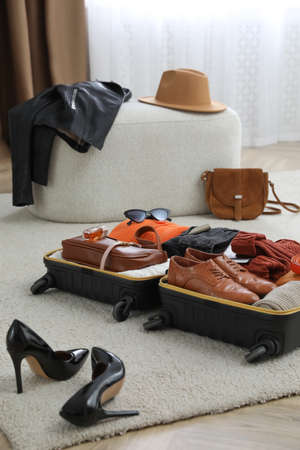 Open suitcase with folded clothes, accessories and shoes on floor indoorsの写真素材