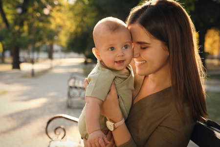 Young mother with her cute baby on bench in parkの写真素材