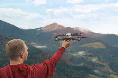 Young man with modern drone in mountains, back view