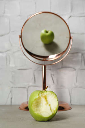 Bitten green apple near mirror with reflection of whole fruit on tableの写真素材