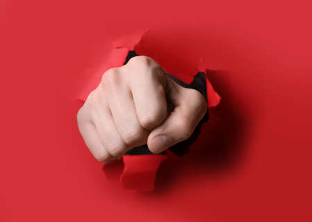 Man breaking through red paper with fist, closeupの写真素材