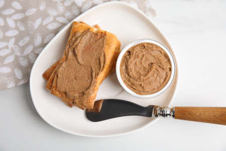 Crispy crackers with delicious meat pate and knife on white table, flat lay