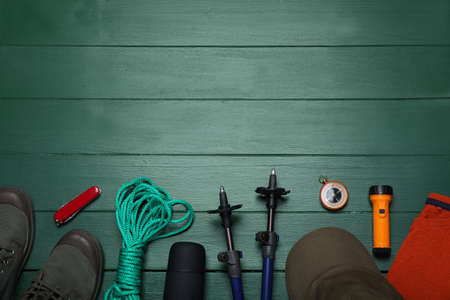 Flat lay composition with trekking poles and other hiking equipment on green wooden background, space for textの写真素材