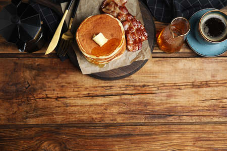 Delicious pancakes with maple syrup, butter and fried bacon on wooden table, flat lay. Space for...