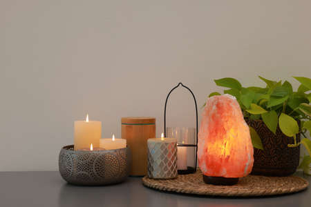 Himalayan salt lamp, houseplant and candles on gray table near light wall, space for textの写真素材