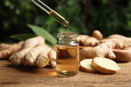 Dripping ginger essential oil from pipette into bottle on wooden tableの写真素材