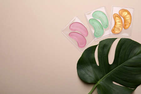 Under eye patches and tropical leaf on beige background, flat lay with space for text. Cosmetic productの写真素材