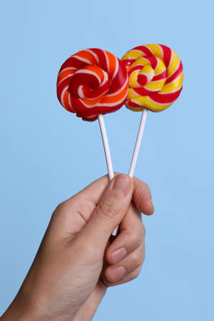 Woman holding bright tasty lollipops on light blue background, closeupの写真素材