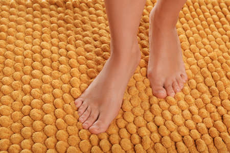 Woman standing on soft orange bath mat, closeup. Space for textの写真素材