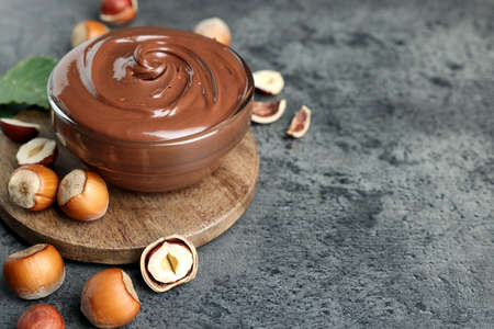 Glass bowl with tasty chocolate hazelnut spread and nuts on gray table. Space for textの写真素材