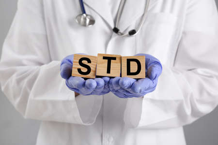 Doctor holding wooden cubes with abbreviation STD on gray background, closeupの写真素材