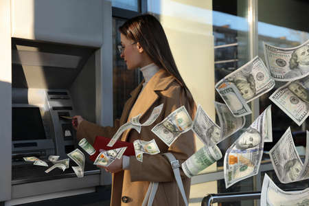 Woman using cash machine and flying money outdoorsの写真素材