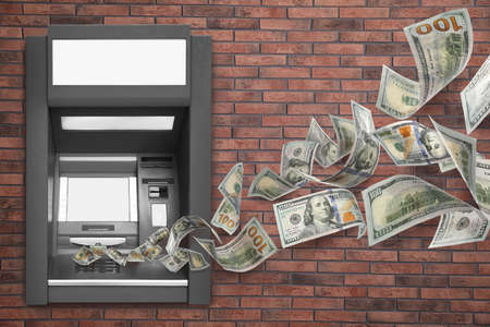 Modern automated cash machine on brick wall and flying moneyの写真素材