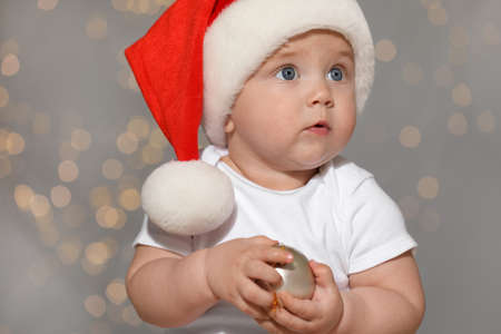 Cute baby in Santa hat with Christmas ball against blurred lightsの写真素材