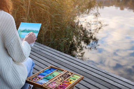 Woman drawing with soft pastels on wooden pier near river, closeupの写真素材