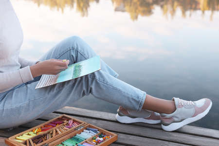 Woman drawing with soft pastels on wooden pier near river, closeupの写真素材