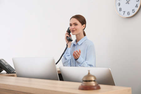 Beautiful receptionist talking on phone at counter in hotelの写真素材