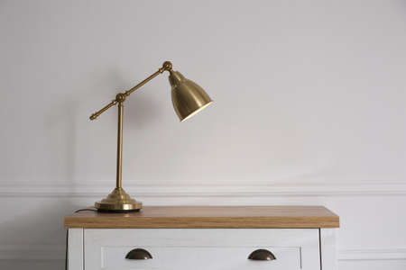 Wooden chest of drawers with modern lamp near white wall, space for text. Interior elementの写真素材